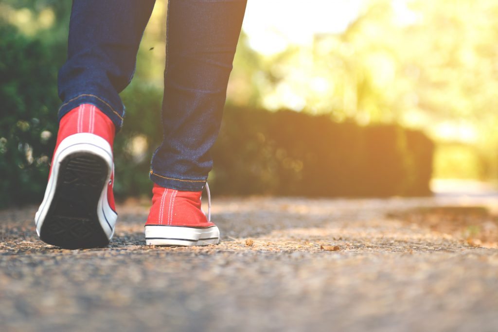 Close up of a person's lower legs and feet, walking with red sneakers outdoors.