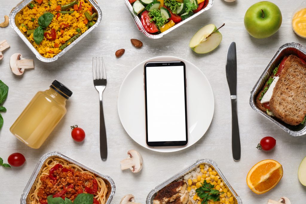 Flat lay composition with lunchboxes and smartphone on white wooden table.