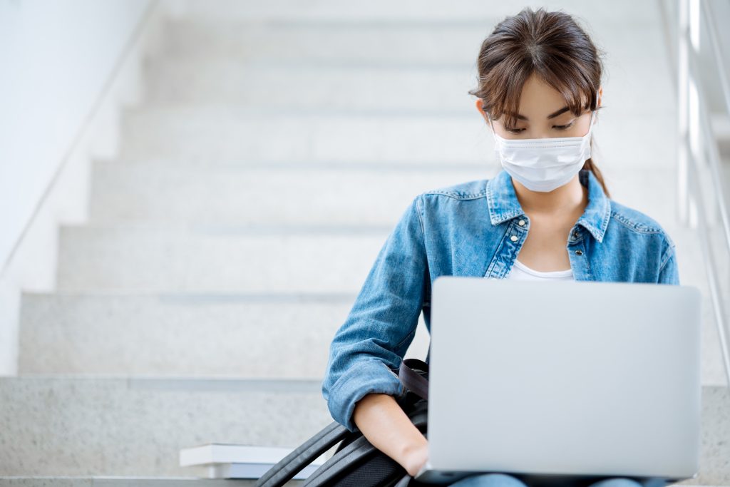 Student wearing mask working on a laptop on stairs at a university campus