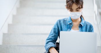 Student wearing mask working on a laptop on stairs at a university campus